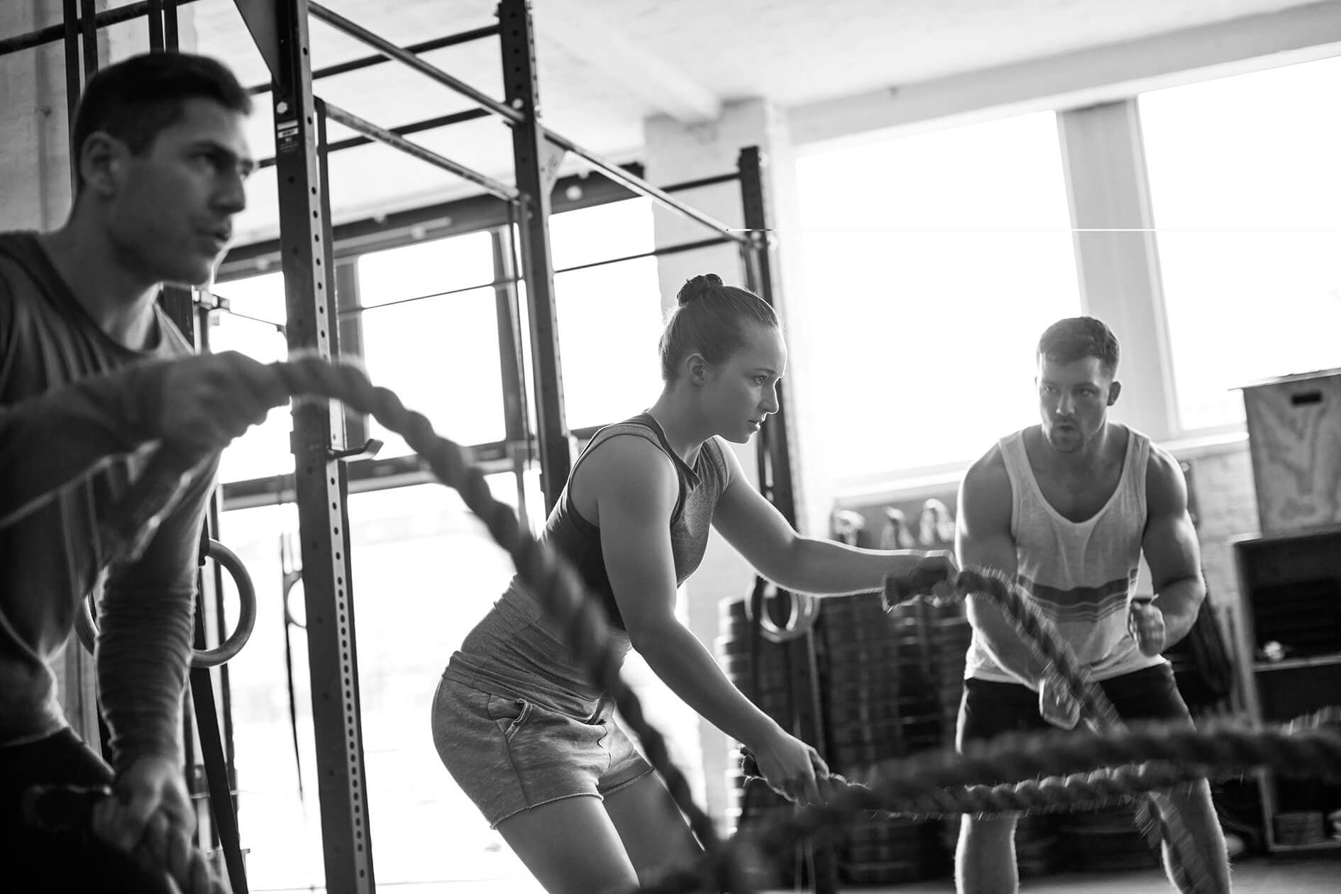Fitness gym with man and woman working out with battle ropes at the gym